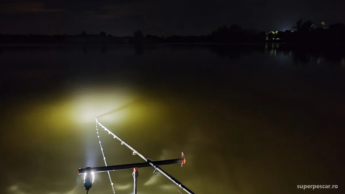 Lansete de crap pe rod pod noaptea, luminate de lanterna frontală, pe un lac întunecat